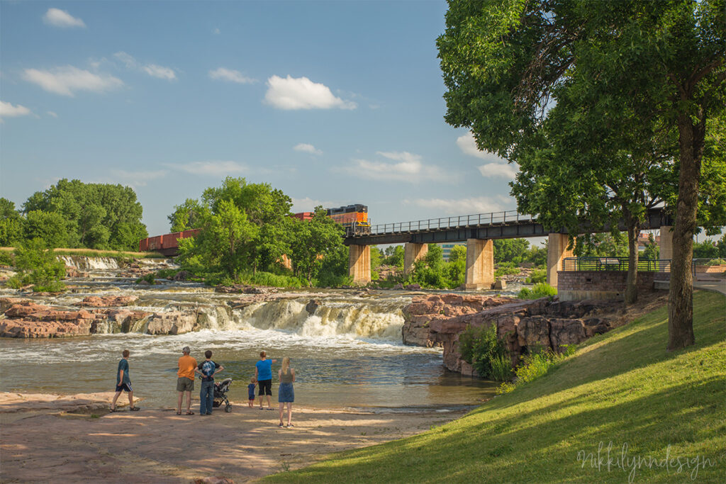 Freight train crossing the bridge above the waterfalls at Falls Park in Sioux Falls, South Dakota with visitors viewing the cascades below.